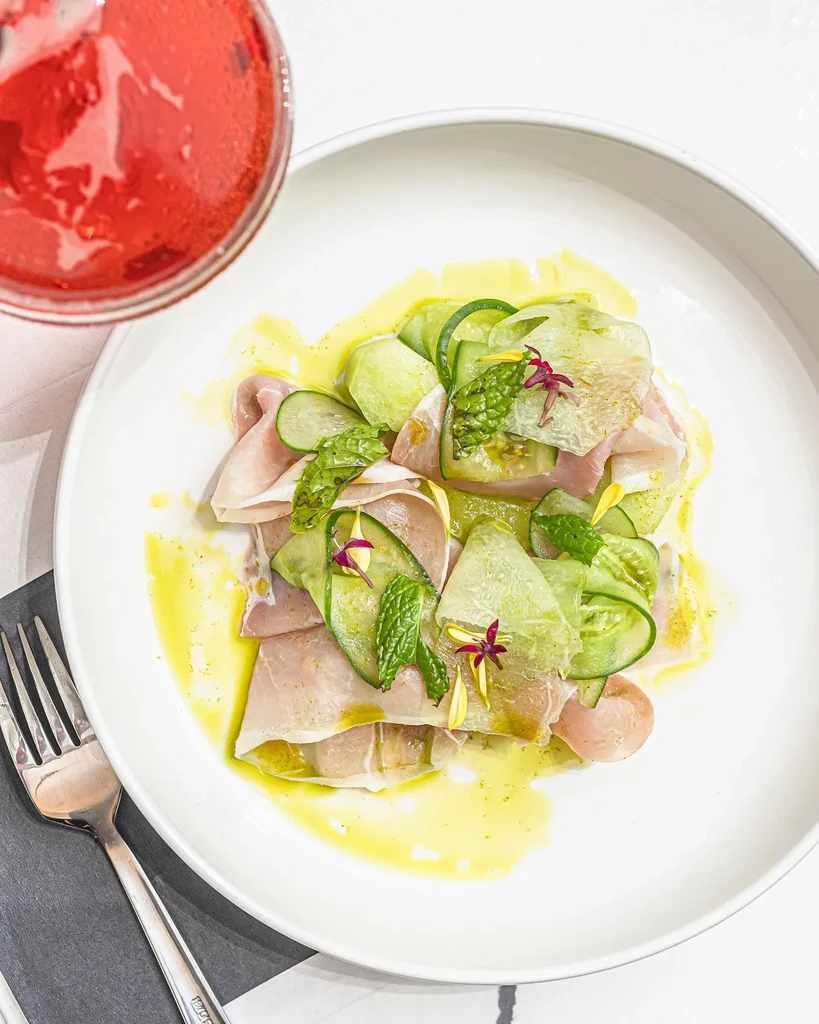 Prosciutto, cucumber, and mint salad with edible flowers and red drink.
