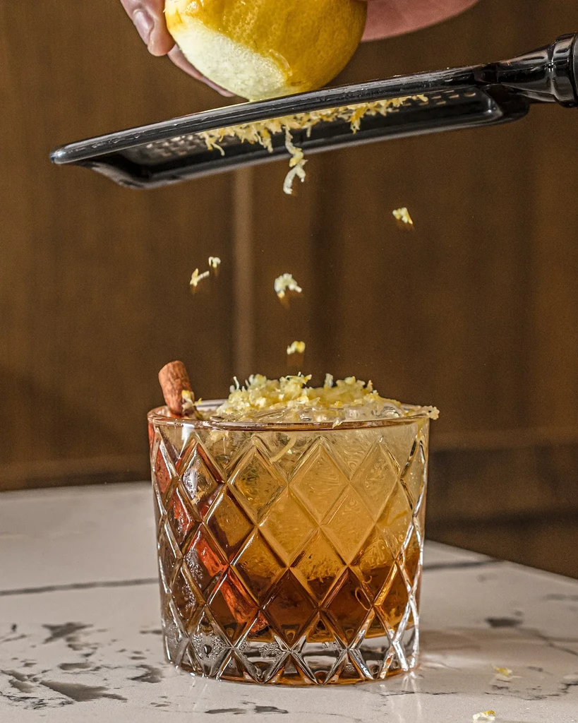 Lemon zest grated over a cocktail in a patterned glass.