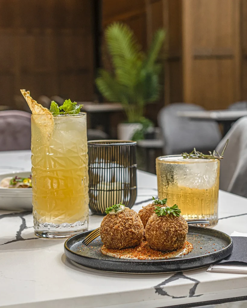 Appetizer plate with three fried balls and two cocktails on a table.