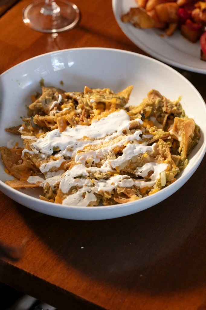 White bowl of chilaquiles with sour cream and shredded cheese.