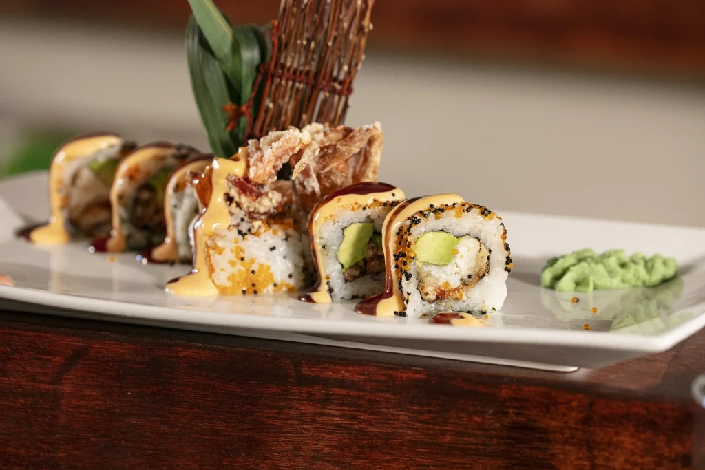 Sushi rolls with avocado and sauce on a white plate with wasabi.