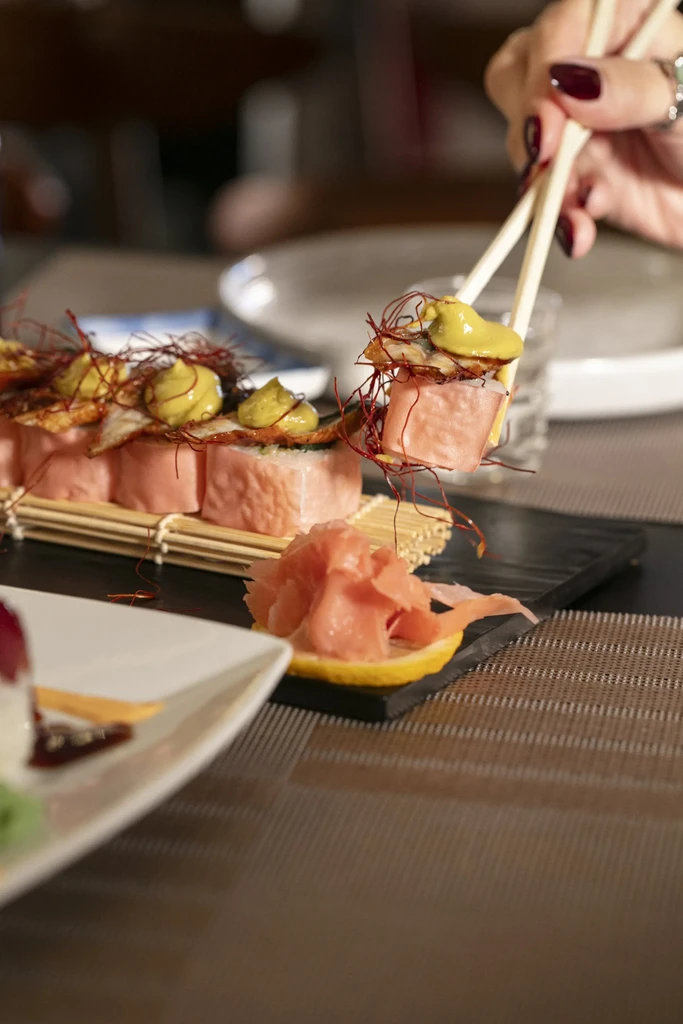 A hand uses chopsticks to pick up a piece of sushi.