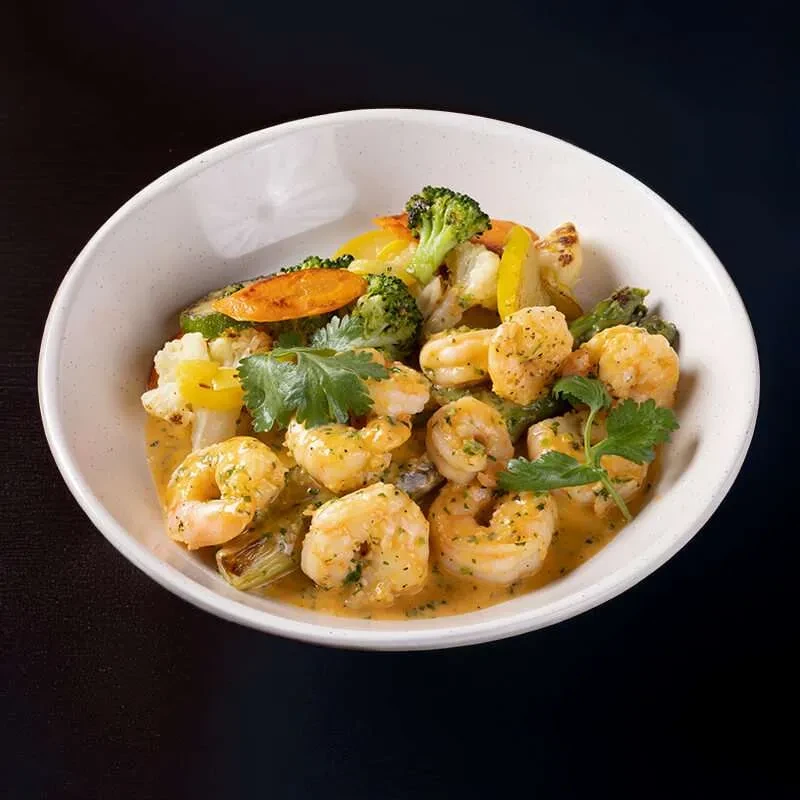 A white bowl filled with shrimp, vegetables, and a creamy sauce.