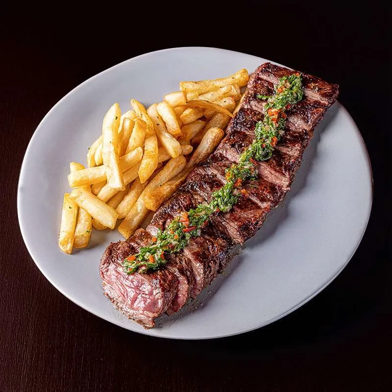 Sliced steak with green chimichurri sauce and golden fries on a plate.