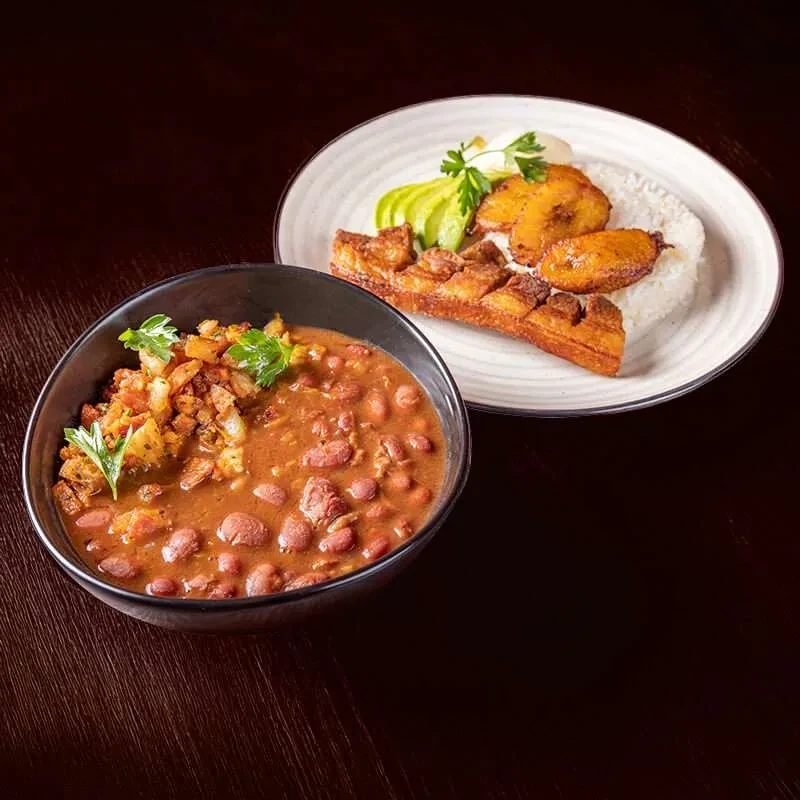 Bowl of red beans and plate with rice, pork belly, and plantains.