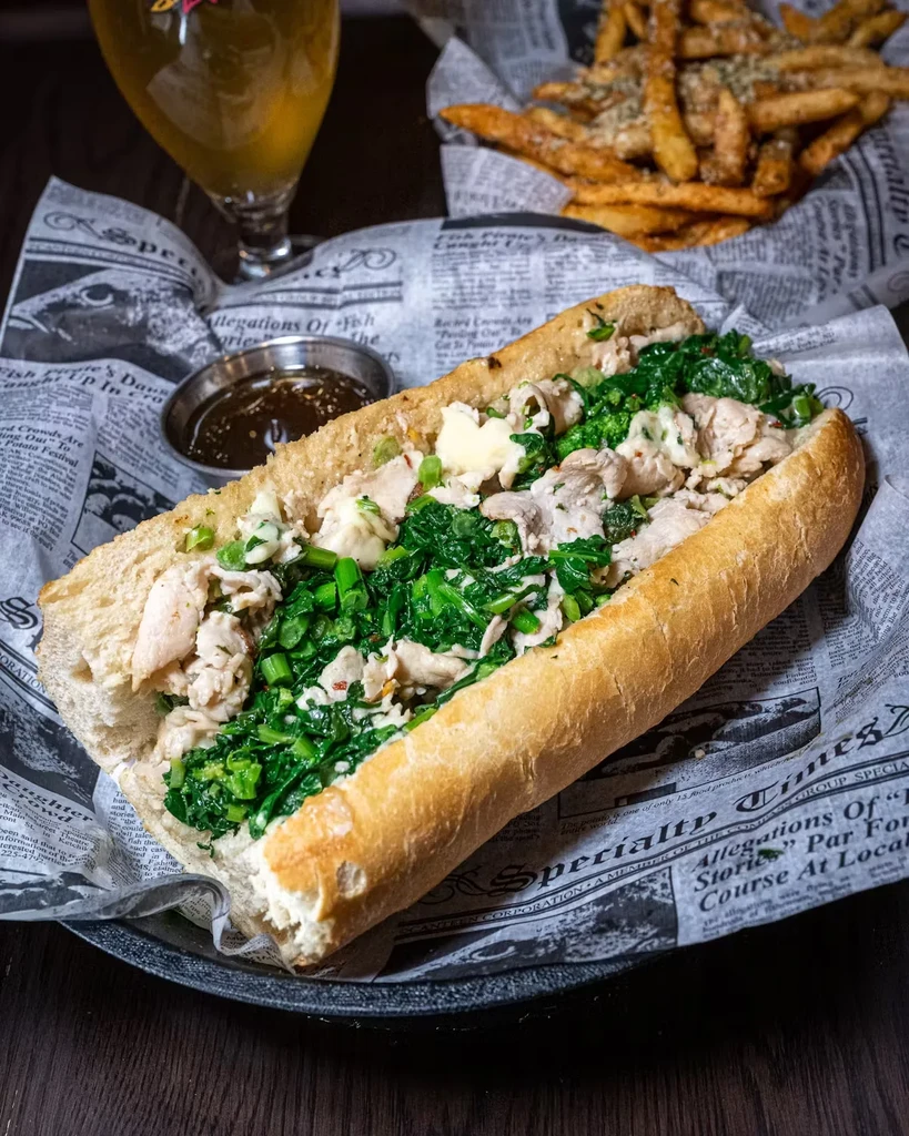 A chicken and greens sandwich with fries, beer, and a dipping sauce.