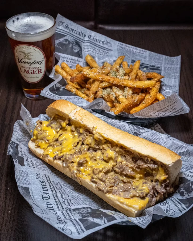 A cheesesteak sub with fries and a glass of Yuengling beer.