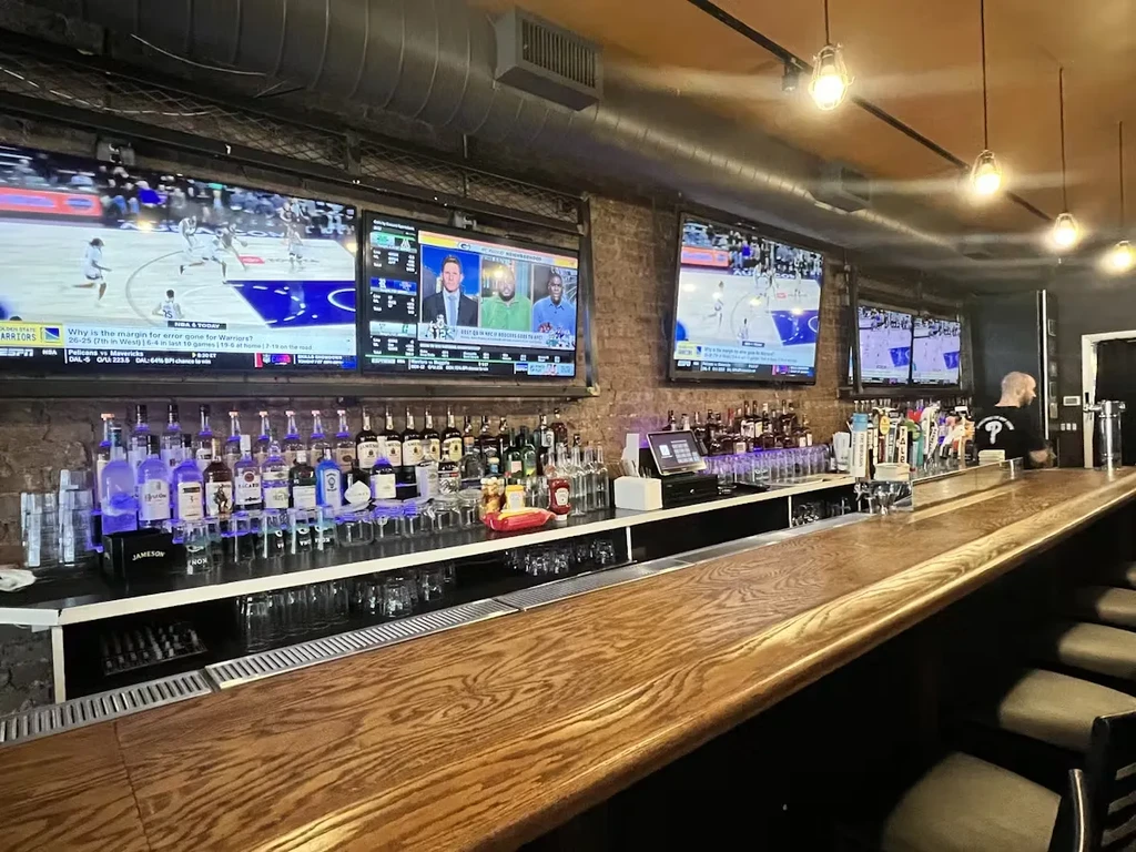 A long, empty wooden bar with multiple TVs showing sports.