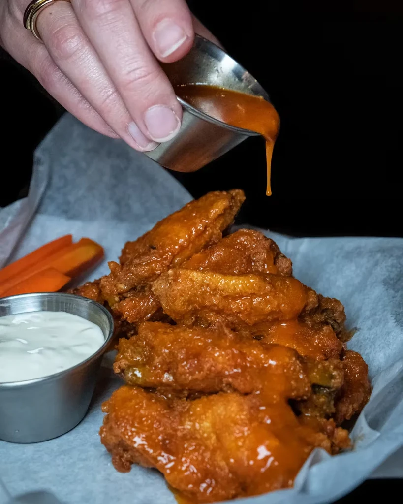 Sauce pours over fried chicken wings with carrots and dip.