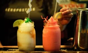 Two frosty beverages in jars are garnished at a bar.