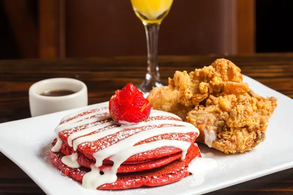 Red velvet pancakes with a strawberry, fried chicken, and a mimosa.