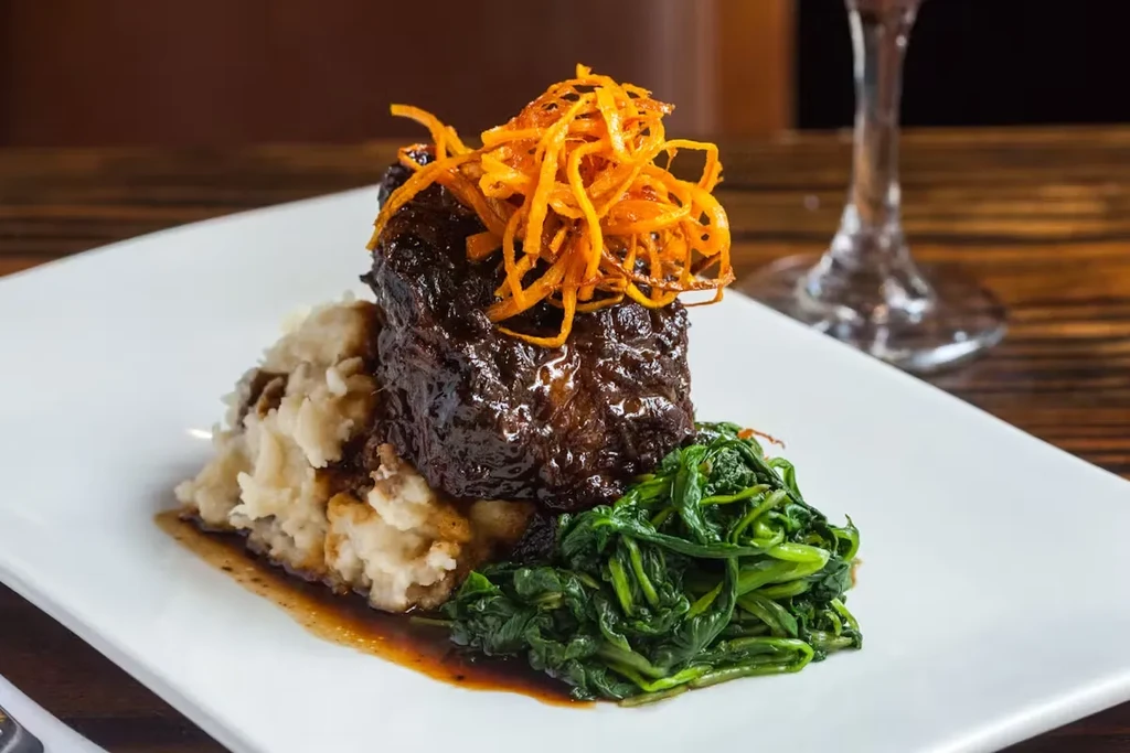 Braised short rib, mashed potatoes, and spinach on a white plate.