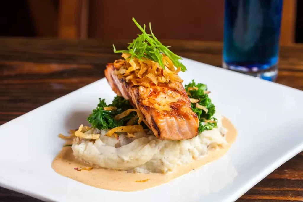 Grilled salmon on mashed potatoes with kale and fried onions.