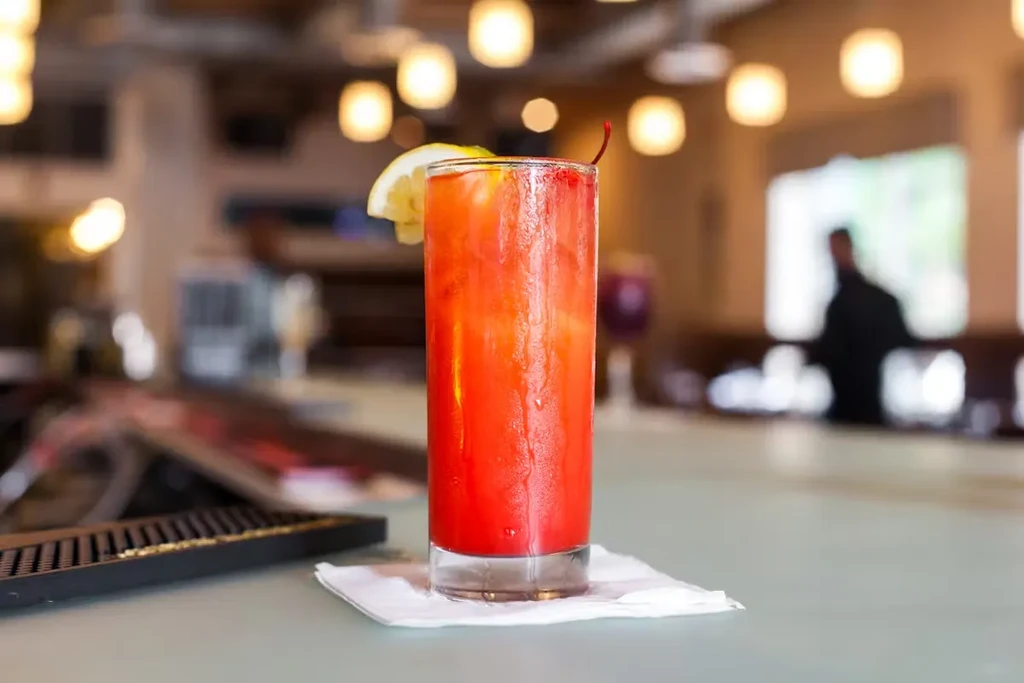 A red cocktail with lemon and cherry on a bar counter.