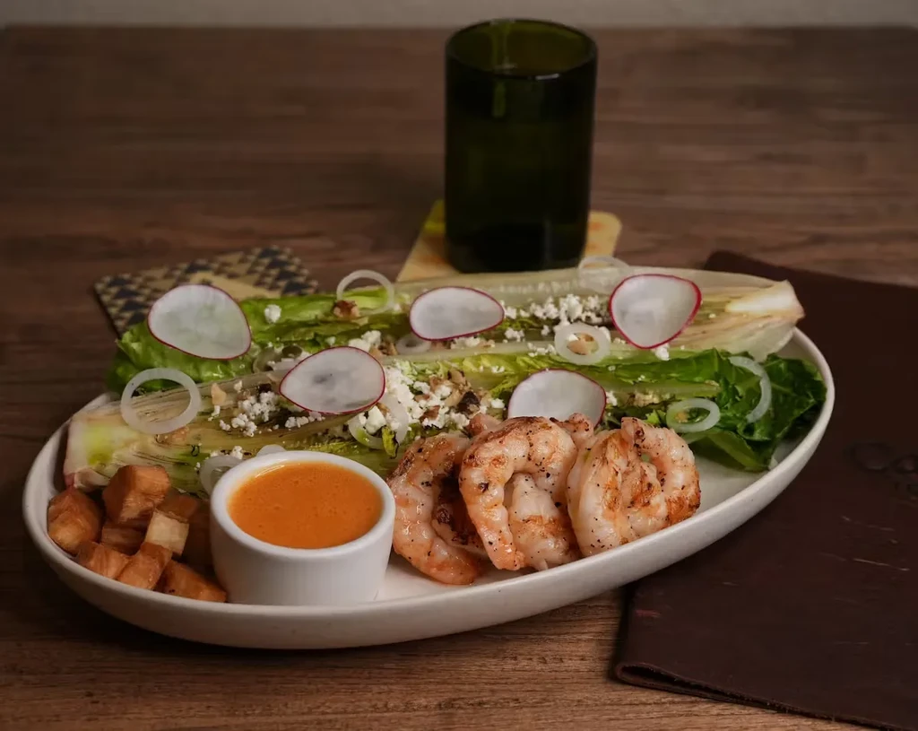 A shrimp salad with radish, onions, and sauce on a white plate.