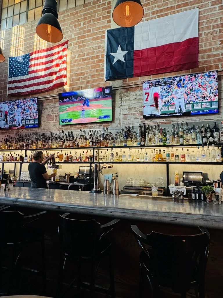 Casual bar interior with bartender, flags, and TVs showing baseball.