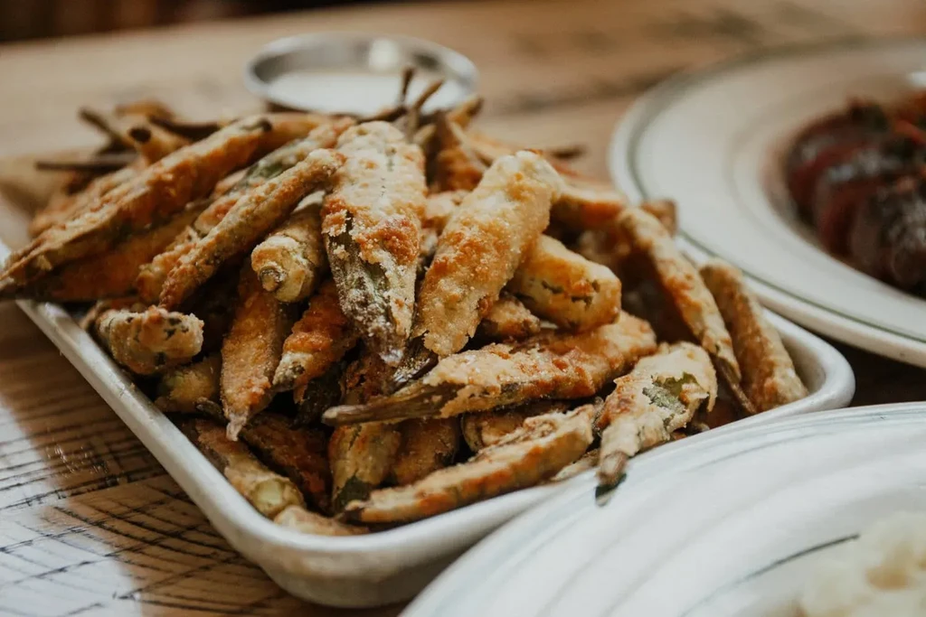 Golden fried okra in white rectangular dish on wooden table.