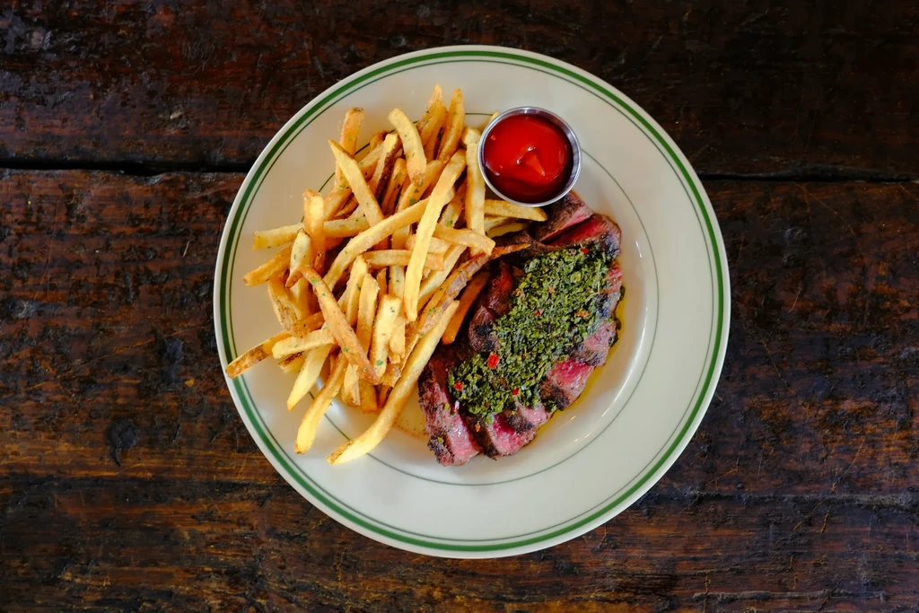 Grilled sliced steak with vibrant green herb sauce, fries, and ketchup.
