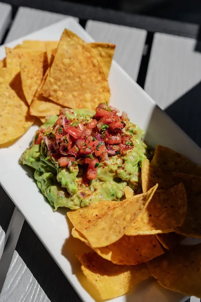 Guacamole with pico de gallo and tortilla chips on a white plate.