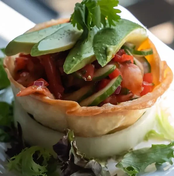 Tortilla cup filled with salsa, topped with avocado slices and cilantro.