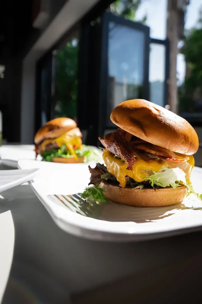 Two bacon cheeseburgers with lettuce and melted cheese on white plates.