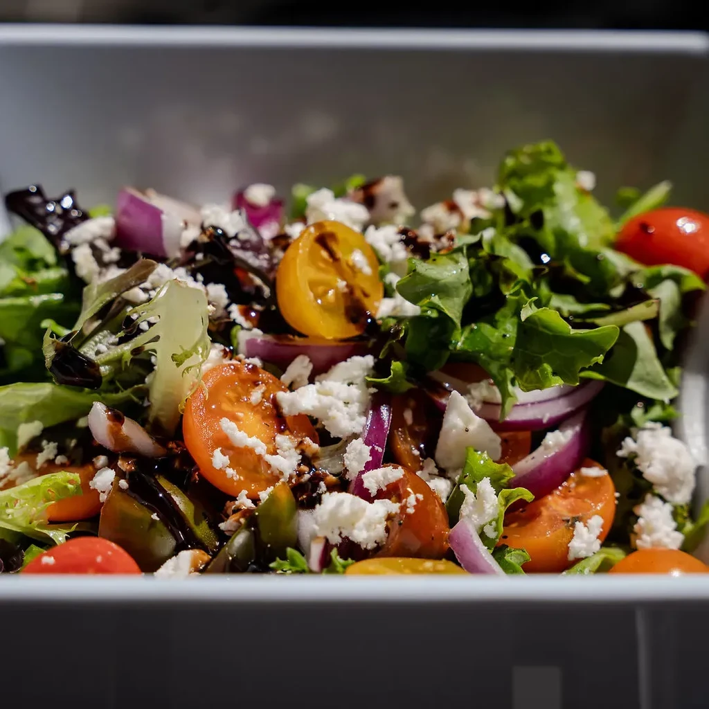 Close-up of fresh green salad with tomatoes, onions, feta, and balsamic.
