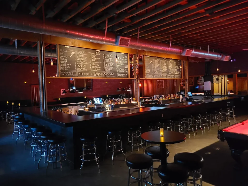Red-lit industrial bar interior with a long counter and menu chalkboards.