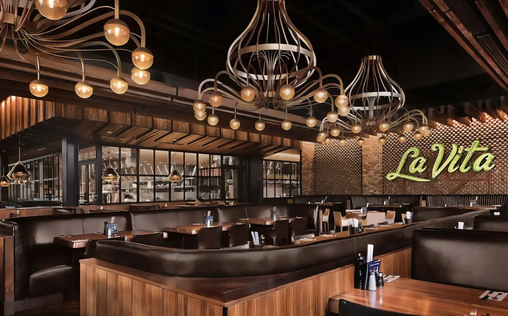 Modern restaurant interior with dark booths, amber chandeliers, and "La Vita" neon sign.