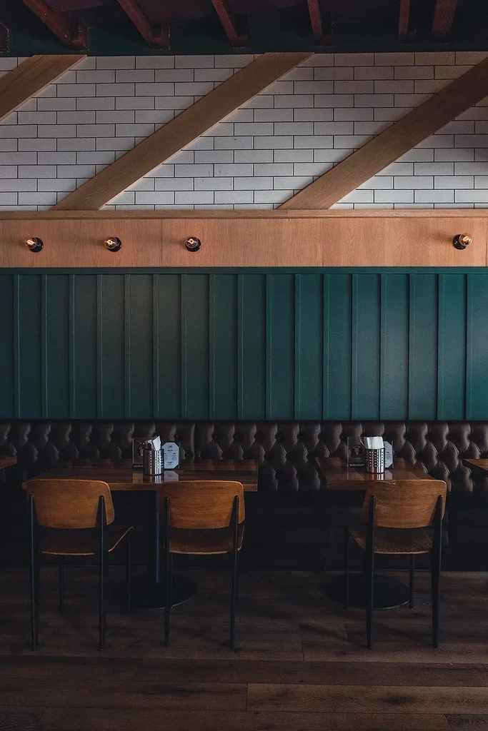 Restaurant interior with dark teal paneling, leather booths, and wooden tables.