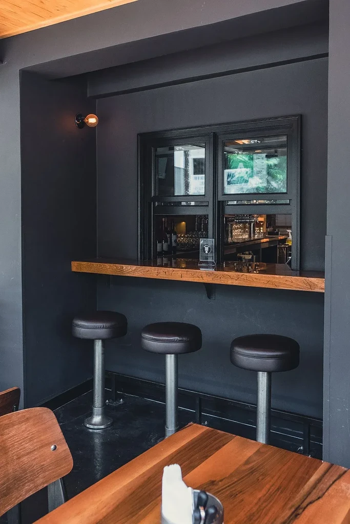 Modern restaurant bar with dark walls, wood counter, three stools.