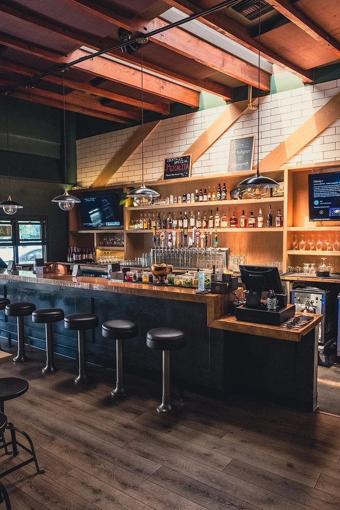 Cozy, modern industrial bar interior with drinks, stools, and wooden beams.