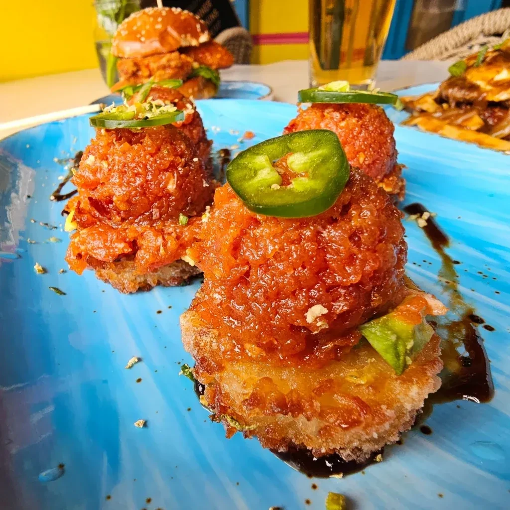 Three crispy spicy tuna tartare appetizers with jalapeño on blue plate.