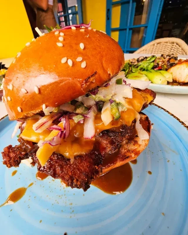 Gourmet burger with melted cheese, red cabbage, dripping sauce on blue plate.