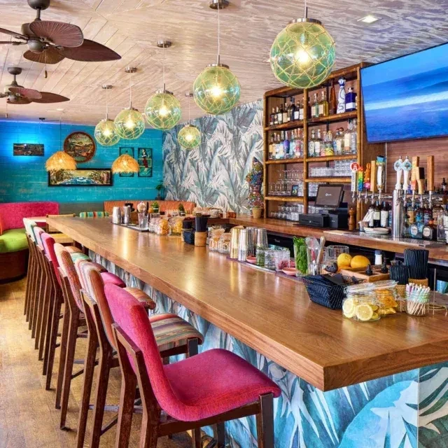 Vibrant tropical bar with wooden counter, green globe lights, and leaf wallpaper.
