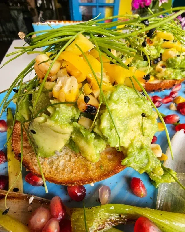 Vibrant avocado toast on blue plate, topped with corn, peppers, chives.