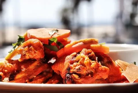 Close-up of spiced chicken, orange vegetables, green herbs, and flatbread.