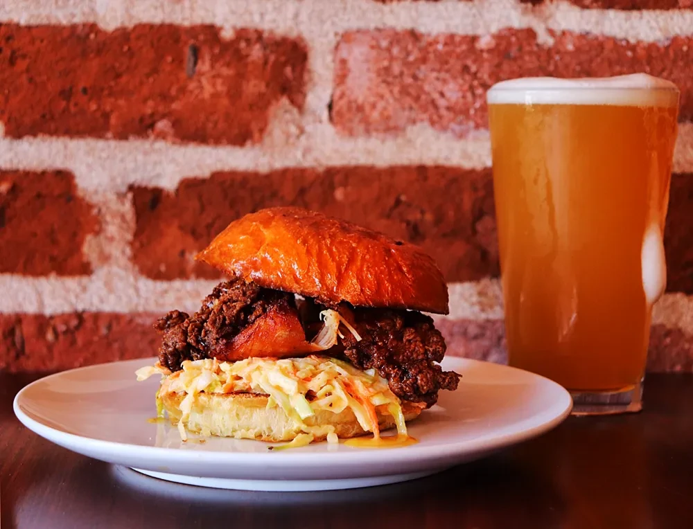 Close-up of a fried chicken sandwich with coleslaw and a beer.