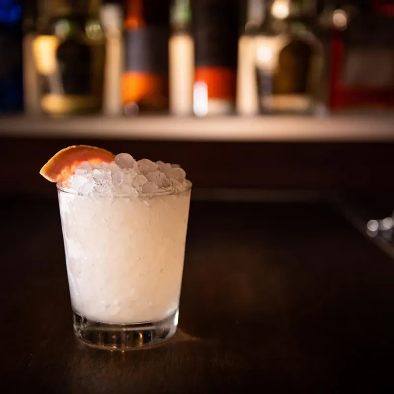 Cocktail with crushed ice and citrus peel in a dimly lit bar.