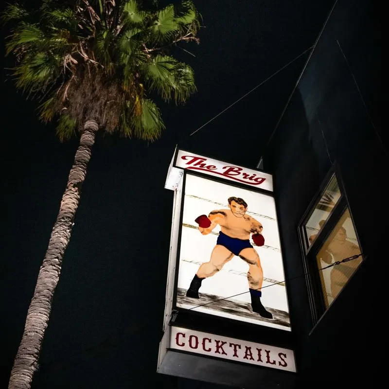 Illuminated "The Brig COCKTAILS" sign showing a boxer at night.