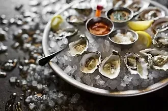 Fresh shucked oysters on a silver platter with ice, lemon, and sauces.