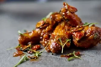 Sticky glazed chicken pieces with herbs on a dark surface.