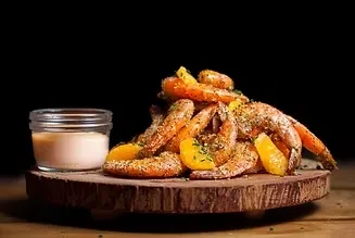 Seasoned shrimp with orange segments, dipping sauce on a wooden board.