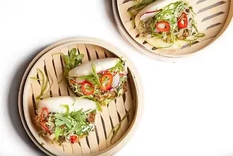 Bamboo steamers hold open-faced bao buns filled with pulled meat and herbs.
