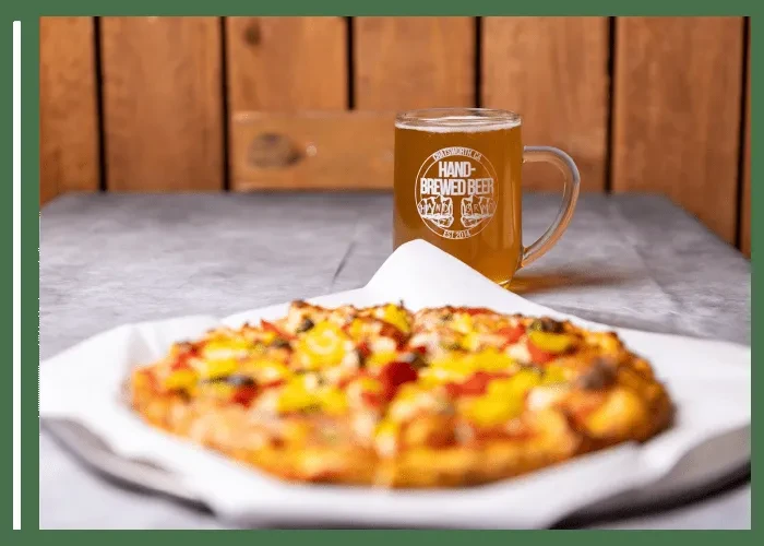 Half-eaten pizza with colorful toppings and a Chatsworth beer mug.