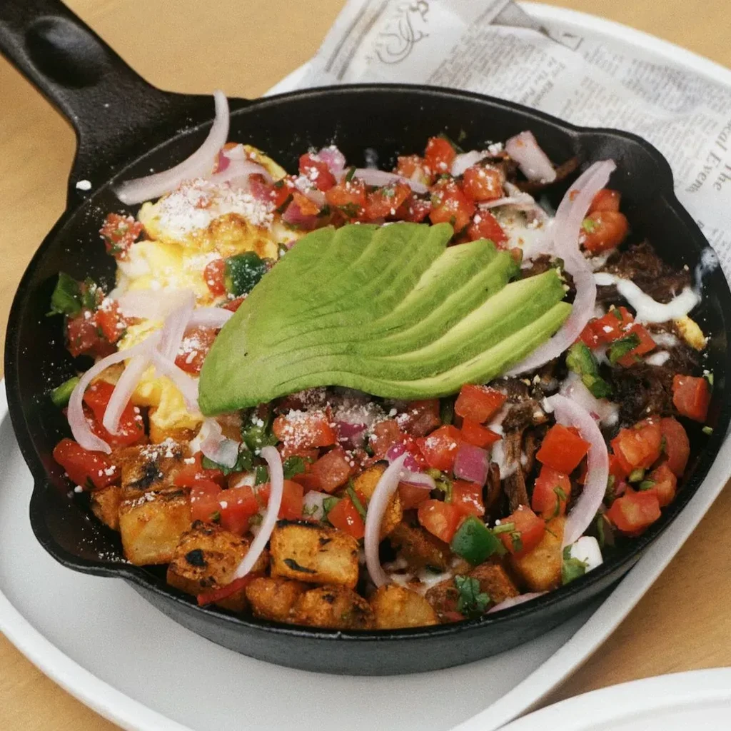 Cast iron skillet with eggs, potatoes, meat, pico de gallo, and avocado.