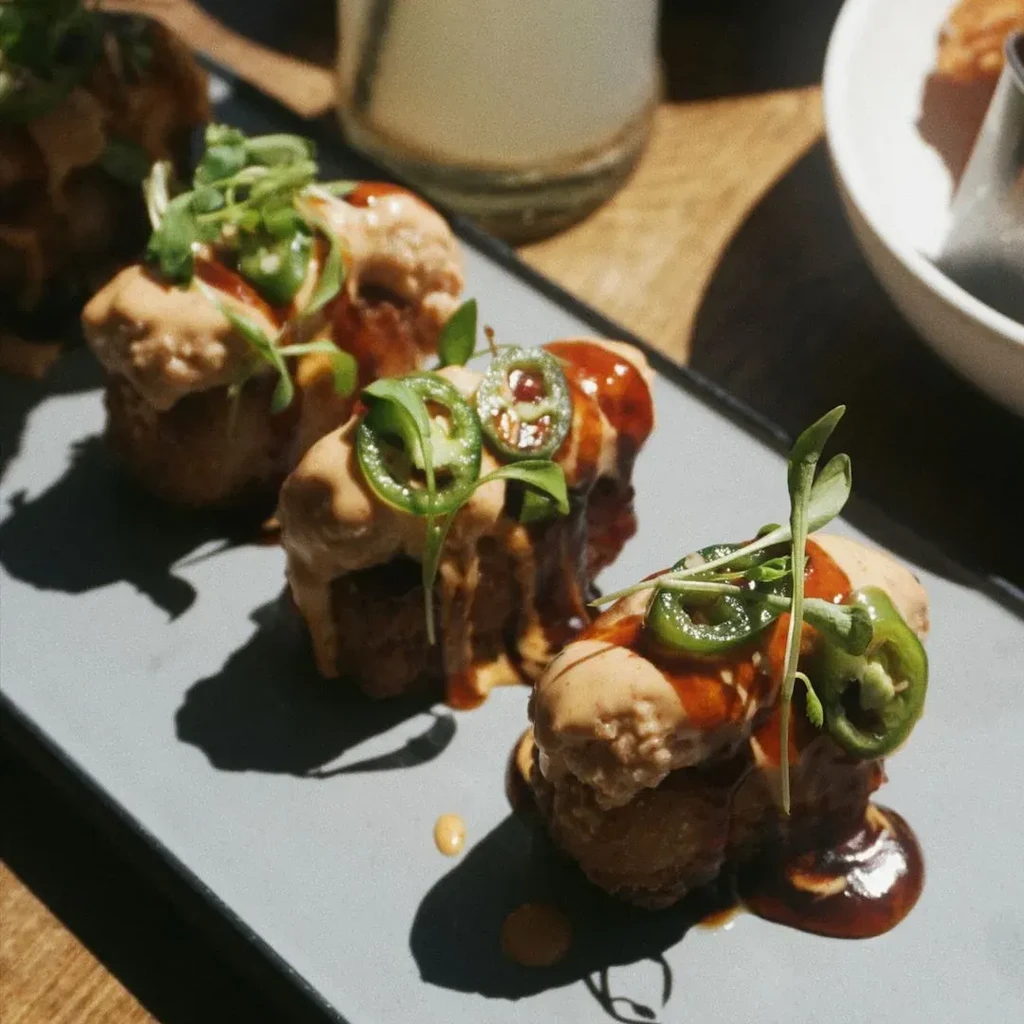 Three fried spheres with sauces, jalapeños, and microgreens on a grey plate.