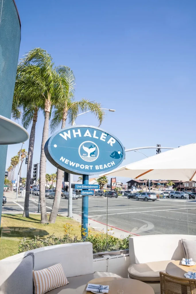 Whaler Newport Beach sign, outdoor patio, palm trees, and busy street.