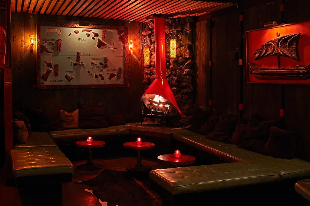 Cozy tiki-themed lounge with a hanging red fireplace and green bench seats.
