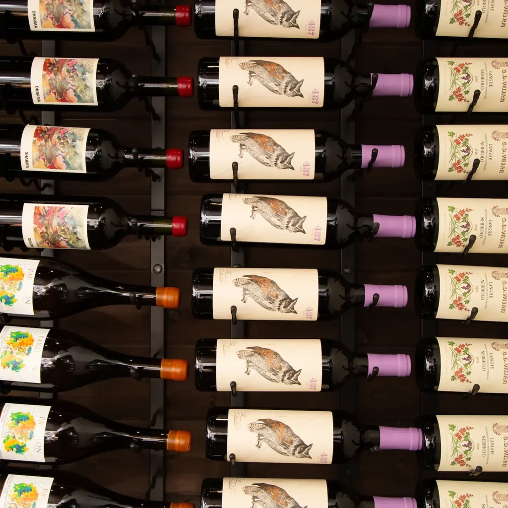 Multiple red wine bottles with distinct labels neatly arranged on a dark rack.