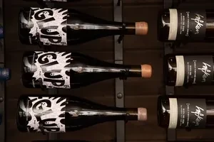 Dark wine bottles with 'GLUP' and 'Hofken' labels on a metal rack.